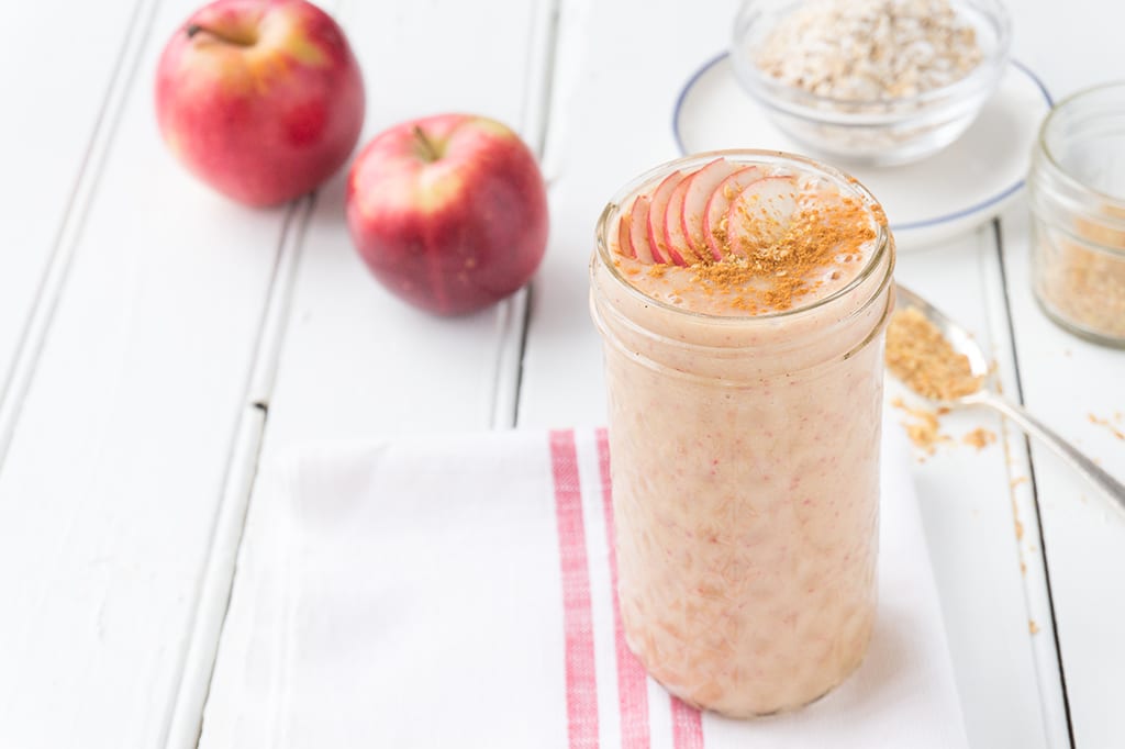 An Apple Oat Smoothie in a glass with apples in the background