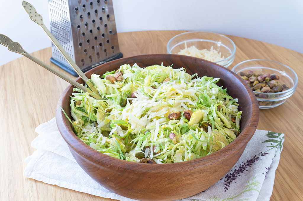 shaved brussels sprouts salad in a wooden bowl with gold utensils