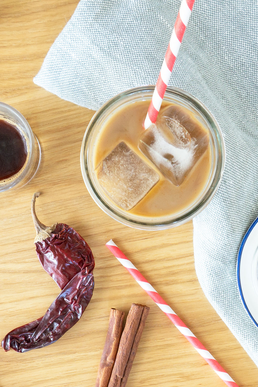 Overhead view of iced mocha with ice cubes and red straw. Chili pepper in backdrop