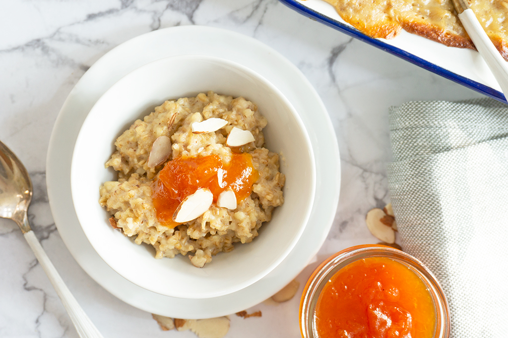 Almond Croissant Vegan Baked Oatmeal in a small bowl with apricot jam and spoon