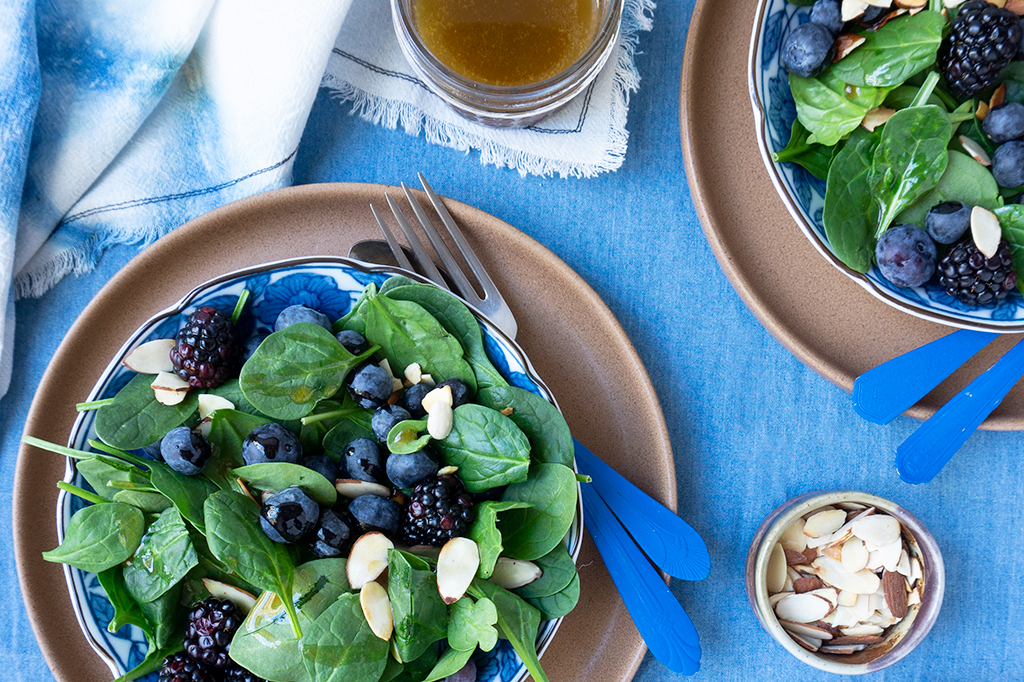 Two plates of berry spinach salad with a side of dressing